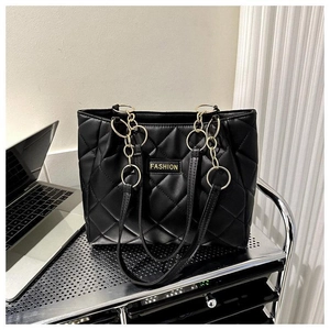 Detail of black quilted tote bag featuring golden chain handles and metal fashion emblem