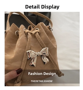 Detail view of beige drawstring bucket bag featuring pleated texture and silver metal bow