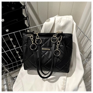 Close-up of black quilted tote bag with golden chain and FASHION label on white blazer
