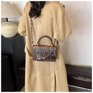 Détail du sac bandoulière à motif léopard avec barre métallique porté par un mannequin
