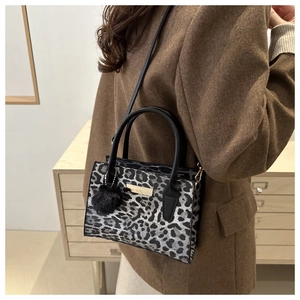 Detail of leopard print handbag featuring gold metal plate and plush black pompom charm