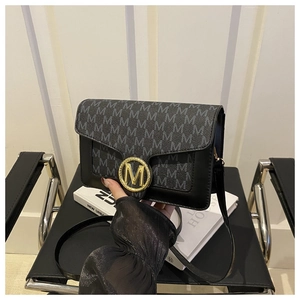 Détail d'un sac bandoulière noir avec imprimé M gris et boucle métallique dorée