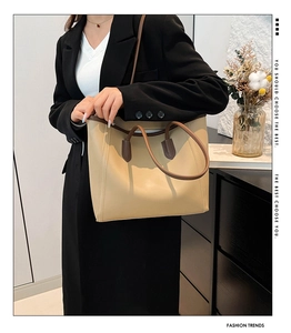 Close-up of a large beige tote bag with brown handles on a model in a black blazer