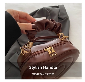 Detailed shot of brown circular quilted handbag featuring pleated handle and gold zippers