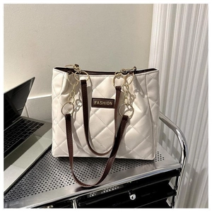 Detail of cream quilted tote bag featuring golden chain rings and brown leather straps