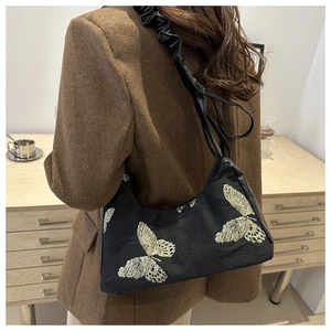 Detailed close-up of a black hobo bag with gold butterfly embroidery and ruffled strap