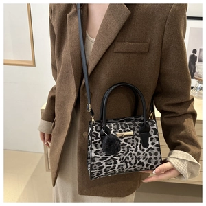 Detail of leopard print crossbody bag with black pompom and gold hardware accessory