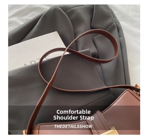 Detail of brown leather crescent bag with golden buckle on a grey blazer fabric