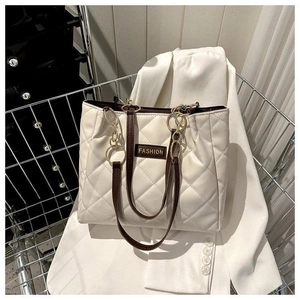 Detail view of a white quilted tote bag featuring a leather patch and golden chain straps