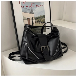 Close-up of black matte tote bag featuring metal buckle strap and diagonal silver zippers