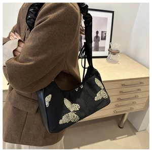 Detail of embroidered gold butterflies on a black canvas underarm bag with pleated strap