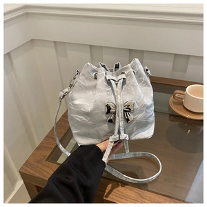 Detail of silver drawstring bucket bag with metallic crinkle texture and bow accent