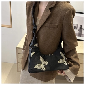 Close-up of golden butterfly embroidery on black canvas bag with ruffled shoulder strap