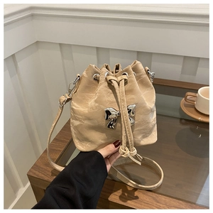 Detail of beige drawstring bucket bag featuring a silver metal bow and pleated texture