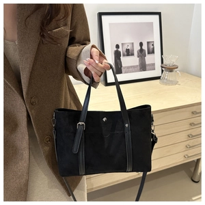 Close-up of black matte tote bag with leather straps and decorative metal buckle details