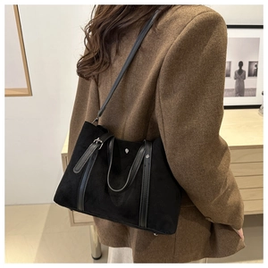 Detail of black tote bag with silver rivets and leather straps held by a model