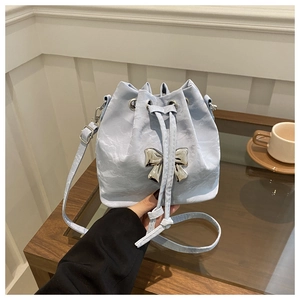 Detail of light blue bucket bag featuring metallic bow buckle and wrinkled leather texture