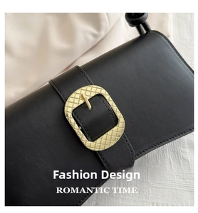 Detail of black leather handbag with a textured gold metallic buckle and grid engraving
