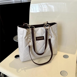 Minimalist white quilted tote bag with brown leather straps and gold chain on a chair
