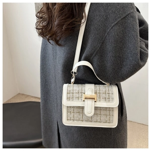 Detail of cream white handbag featuring green tweed flap and gold buckle on a grey coat