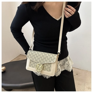 Détail du sac à bandoulière beige à lettres avec une boucle dorée en M sur le rabat