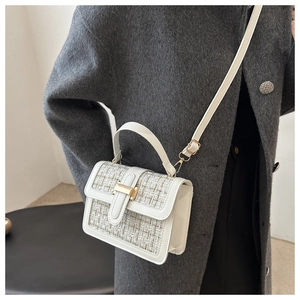Close-up of a white tweed crossbody bag with gold lock buckle and adjustable strap
