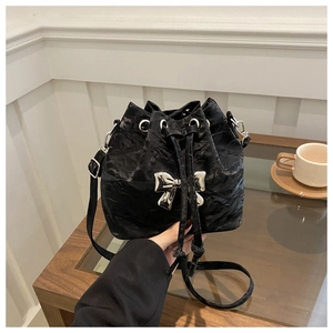 Close-up of black pleated bucket bag featuring a large silver metal bow and drawstring