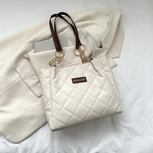 Quilted off-white tote bag with gold chain handles and fashion logo on beige blazer