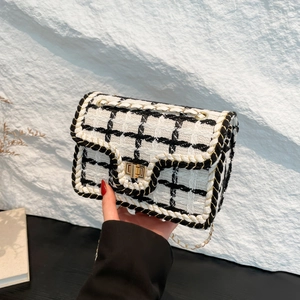 Elegante borsa a tracolla in tweed bianco e nero con catena dorata su sfondo materico
