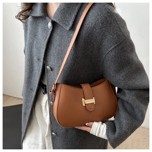 Brown half-moon baguette bag with gold buckle worn on shoulder over a grey wool coat