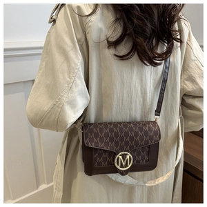 Détail du sac à bandoulière marron vintage avec imprimé lettres et boucle dorée en M
