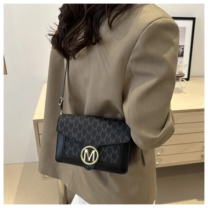 Sac bandoulière rétro noir avec fermoir doré en M et motif monogramme porté par mannequin