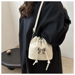 Detail of a beige drawstring bucket bag with a silver metallic bow on a black coat