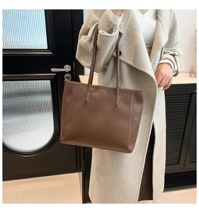 Detail of dark brown matte leather tote bag with vertical stitching on a grey wool coat