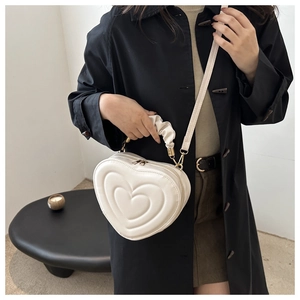 Detail der cremefarbenen herzförmigen Handtasche mit Steppmuster und gerafftem Griff am Model