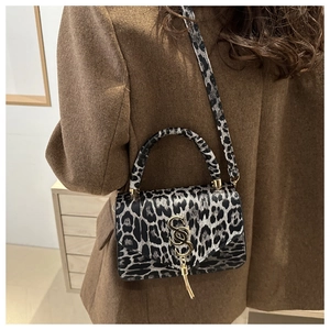 Détail du sac à bandoulière léopard tendance avec logo doré porté sur un manteau brun