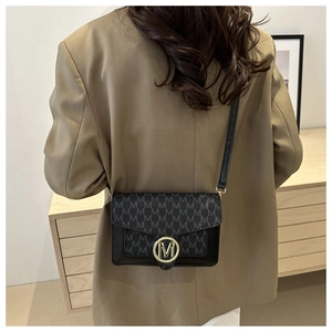 Vue latérale d'une femme portant un sac bandoulière noir avec imprimé et logo M