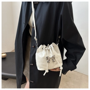 Detail of pearl white drawstring bucket bag with silver butterfly metal buckle on black coat