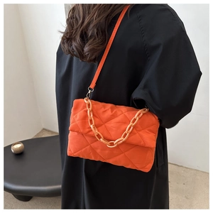 Détail du sac bandoulière matelassé orange vif avec grosse chaîne sur un manteau noir