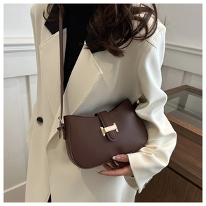 Detail of dark brown semi-circle saddle bag with gold H-buckle worn on white blazer