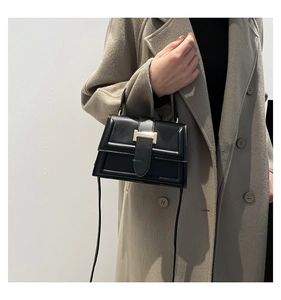 Close-up of black leather crossbody bag with gold metal clasp and top handle detail