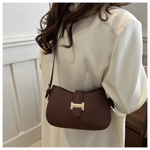 Brown faux leather saddle bag with gold metal buckle shown worn by a model in a beige suit
