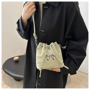 Detail of light green bucket bag with silver bow accent and drawstring on a model