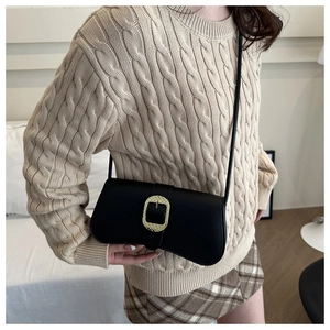 Detail of a black crescent shoulder bag featuring a large textured gold metal buckle
