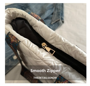 Detail of smooth gold zipper and white quilted satin fabric on a stylish tote bag
