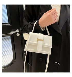 Close-up of white structured square handbag with golden H-shaped clasp and fine stitching