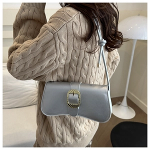 Détail du sac baguette gris argent avec boucle dorée et bandoulière nouée sur pull