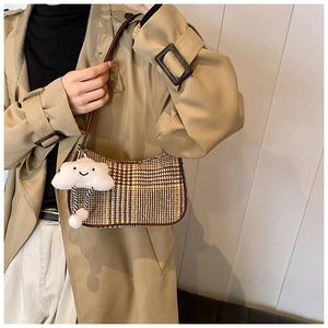 Detail of checkered hobo bag with cloud plush pendant and brown leather trim on trench coat