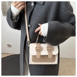 Detailed view of women's beige and khaki crossbody bag on a dark wool coat