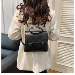 Model wearing a black retro leather backpack with double buckles over a white suit blazer